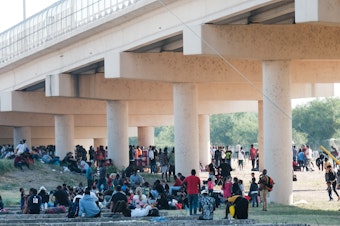 caption: Migrants at the Rio Grande near the port of entry in Del Rio, Texas, on Saturday.
