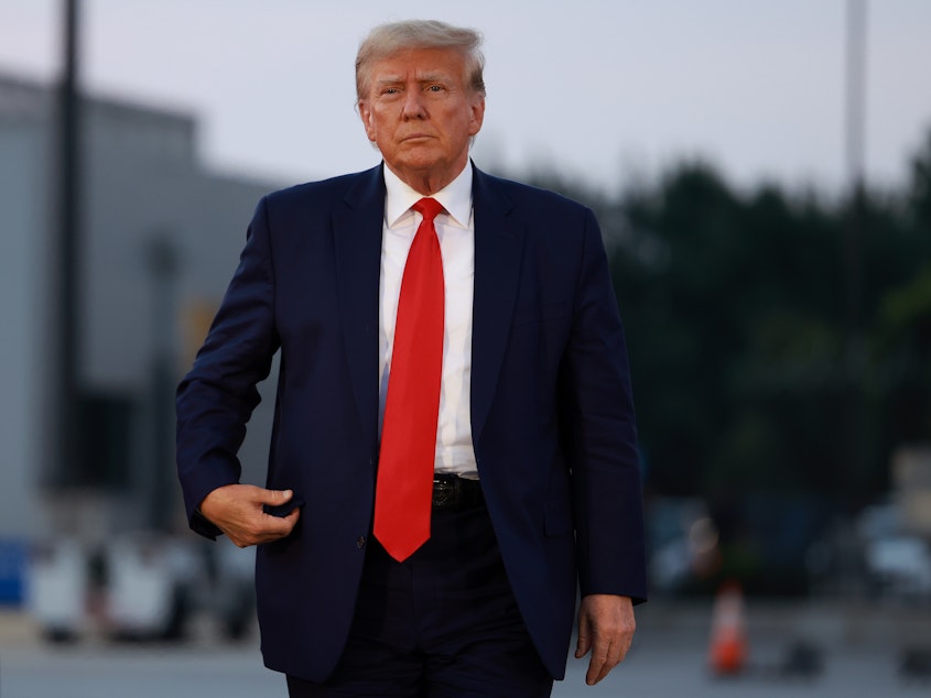 caption: Former President Donald Trump arrives at Atlanta Hartsfield-Jackson International Airport after being booked at the Fulton County jail on Aug. 24.