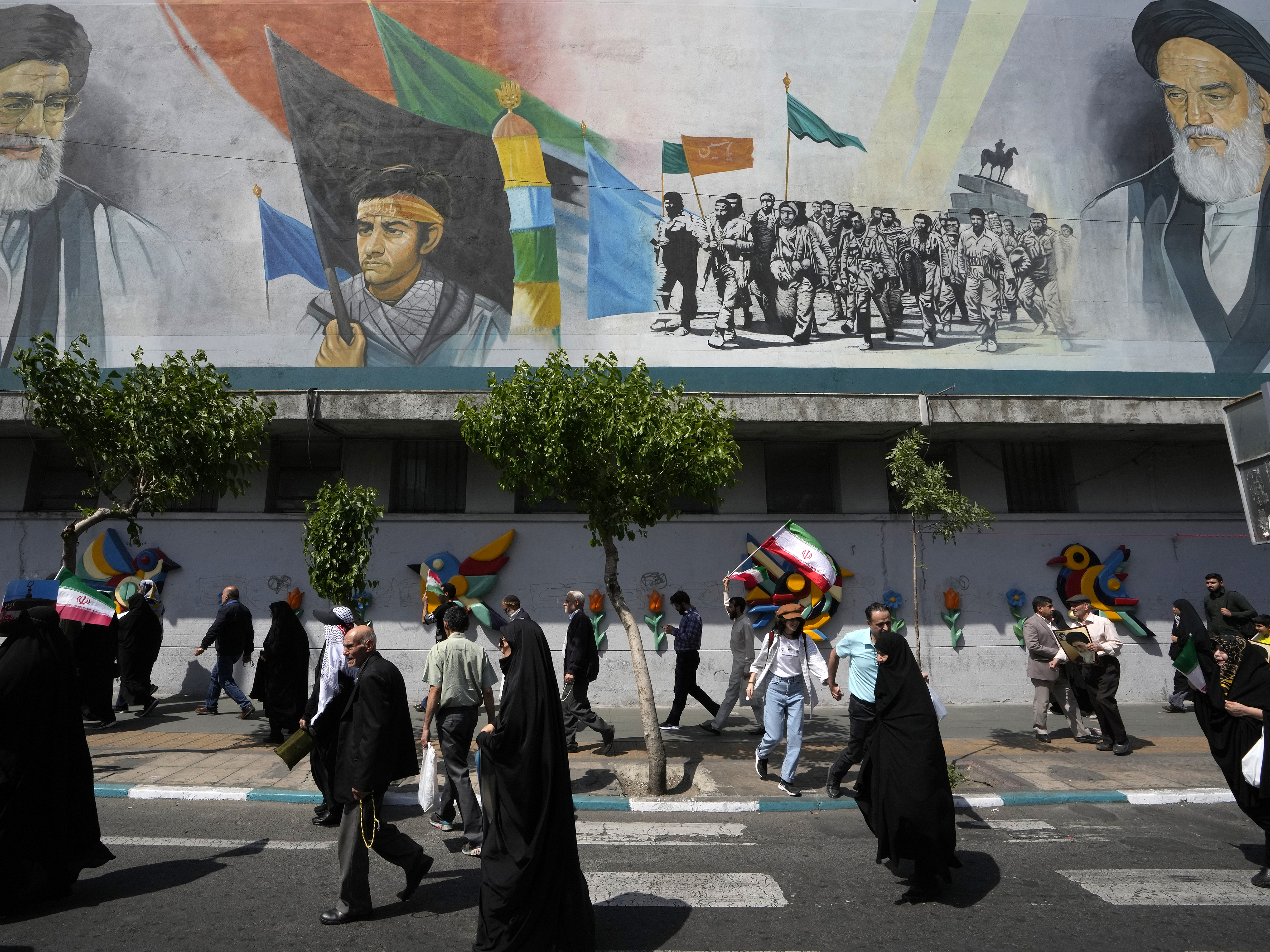 caption: Iranian worshippers walk past a mural showing the late revolutionary founder Ayatollah Khomeini, right, Supreme Leader Ayatollah Ali Khamenei, left, and Basij paramilitary force, in an anti-Israeli gathering after their Friday prayer in Tehran, Iran, on Friday.