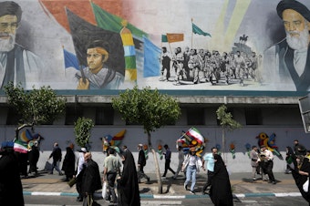 caption: Iranian worshippers walk past a mural showing the late revolutionary founder Ayatollah Khomeini, right, Supreme Leader Ayatollah Ali Khamenei, left, and Basij paramilitary force, in an anti-Israeli gathering after their Friday prayer in Tehran, Iran, on Friday.