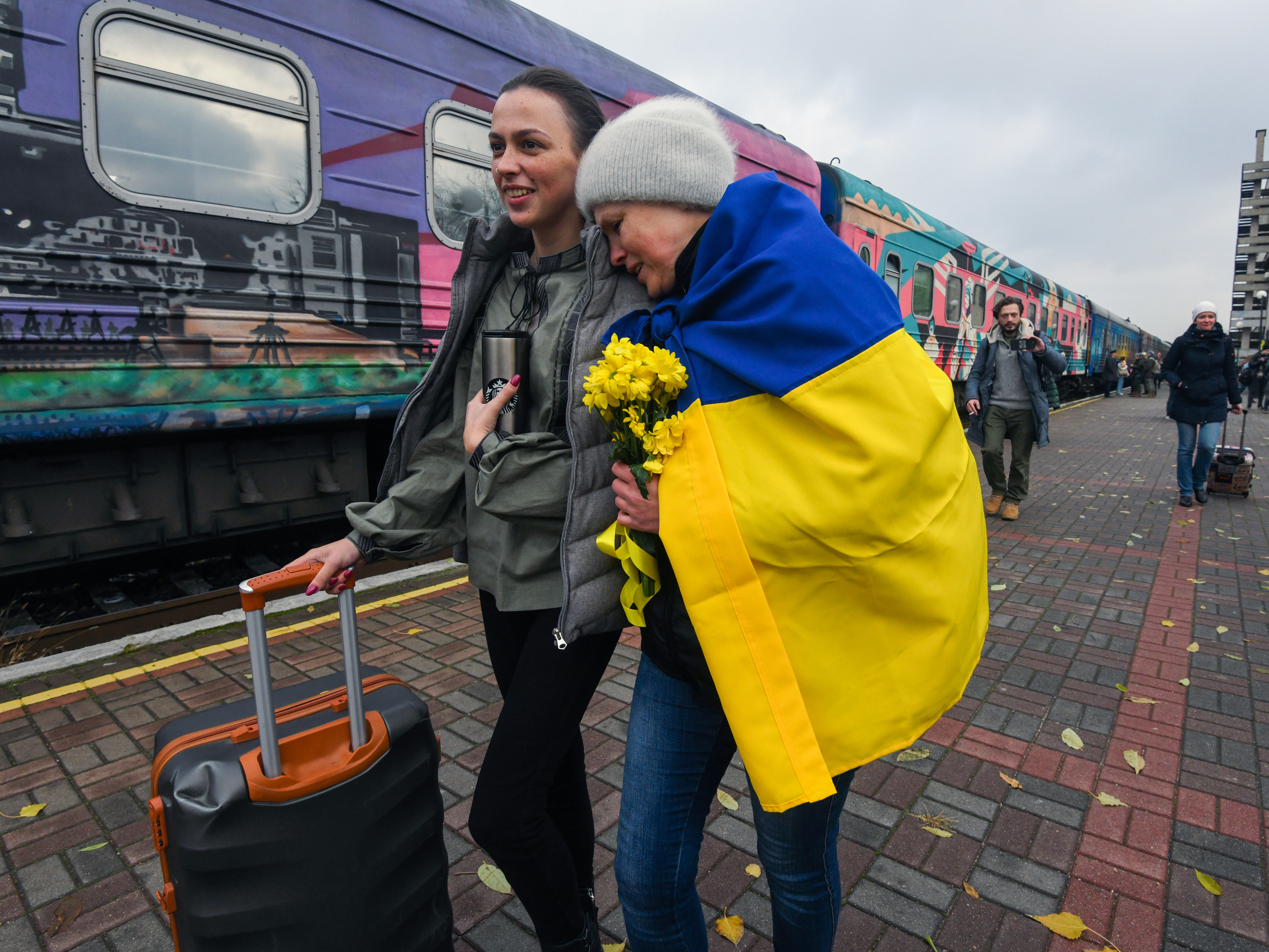caption: Oksana Shevliuha, 51, wears a Ukrainian flag as she greets her daughter, Anastasia, who arrived on the first train to reach liberated Kherson on Saturday. They had not seen each other for six months. The first Ukrainian Railways train arrived in Kherson following a Russian occupation that lasted more than eight months.