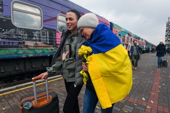 caption: Oksana Shevliuha, 51, wears a Ukrainian flag as she greets her daughter, Anastasia, who arrived on the first train to reach liberated Kherson on Saturday. They had not seen each other for six months. The first Ukrainian Railways train arrived in Kherson following a Russian occupation that lasted more than eight months.