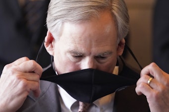 caption: In in this March 17, 2021 file photo, Texas Gov. Greg Abbott removes his mask before speaking at a news conference on in Dallas.