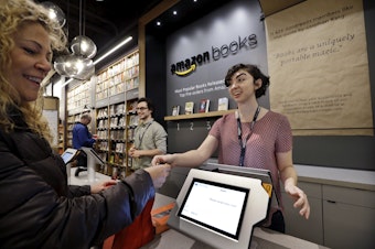 caption: Customer Kirsty Carey, left, gets ready to swipe her credit card for clerk Marissa Pacchiarotti, as she makes one of the first purchases at the opening day for Amazon Books, the first brick-and-mortar retail store for online retail giant Amazon, Tuesday, Nov. 3, 2015, in Seattle.