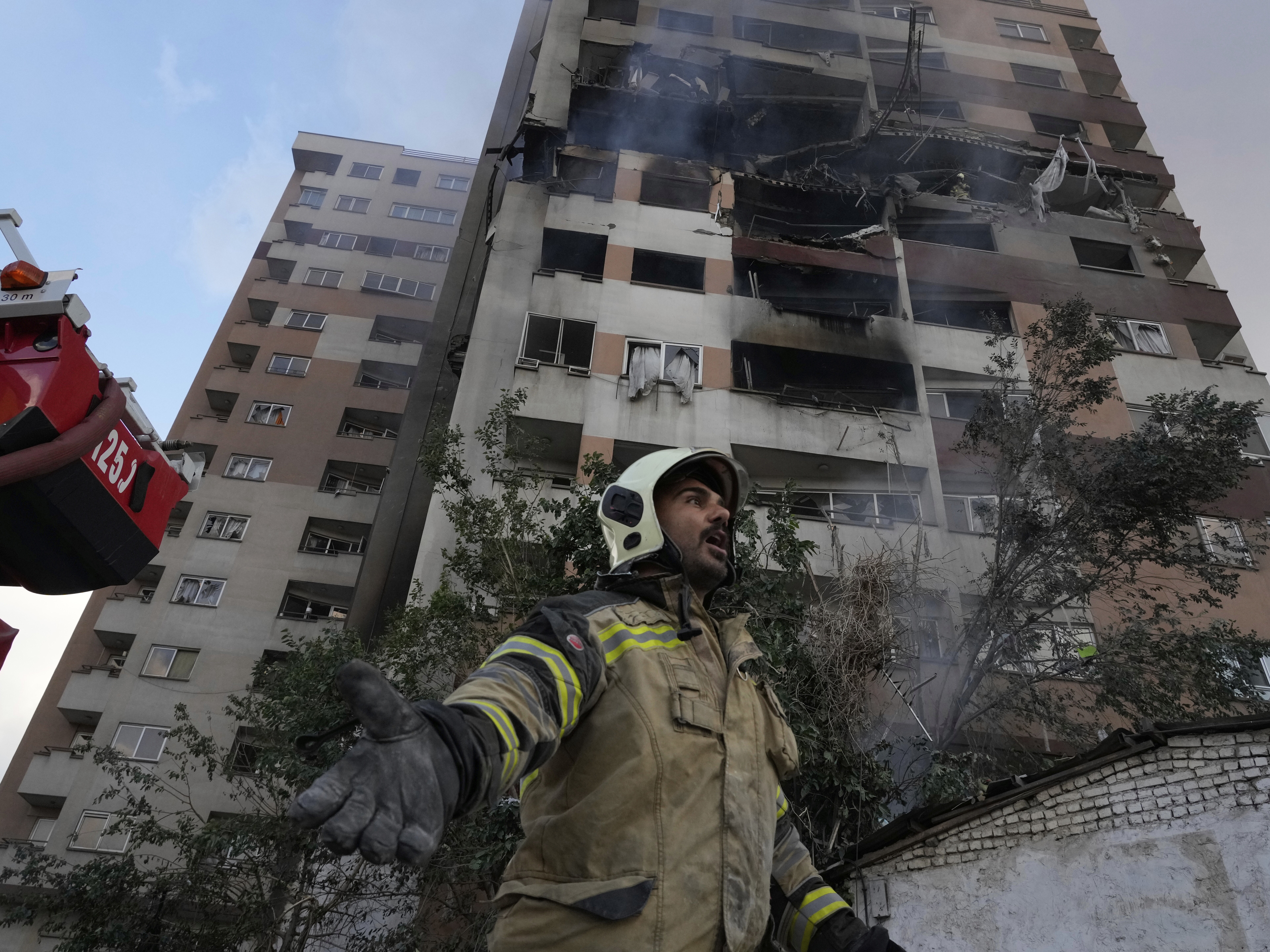 caption: A firefighter calls out his colleagues at the scene of an explosion in a residence compound in northern Tehran, Iran, Friday, June 13, 2025.