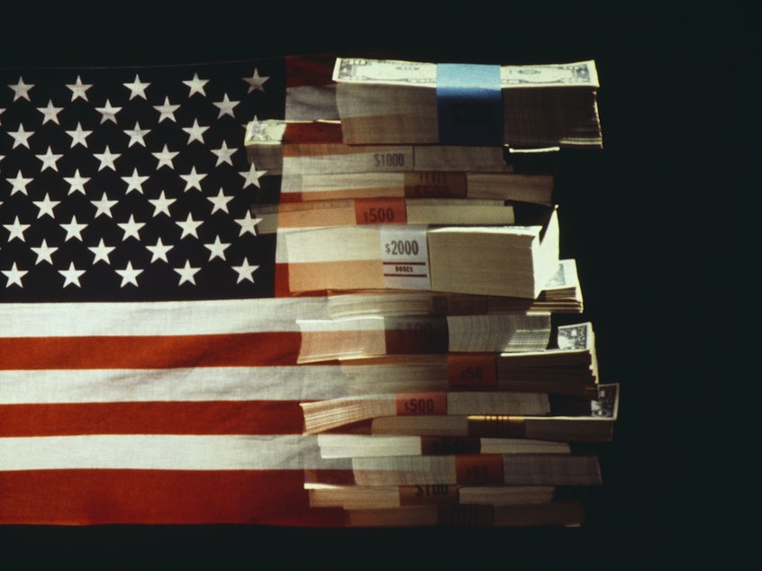 The American flag superimposed over a pile of U.S. dollar banknotes.