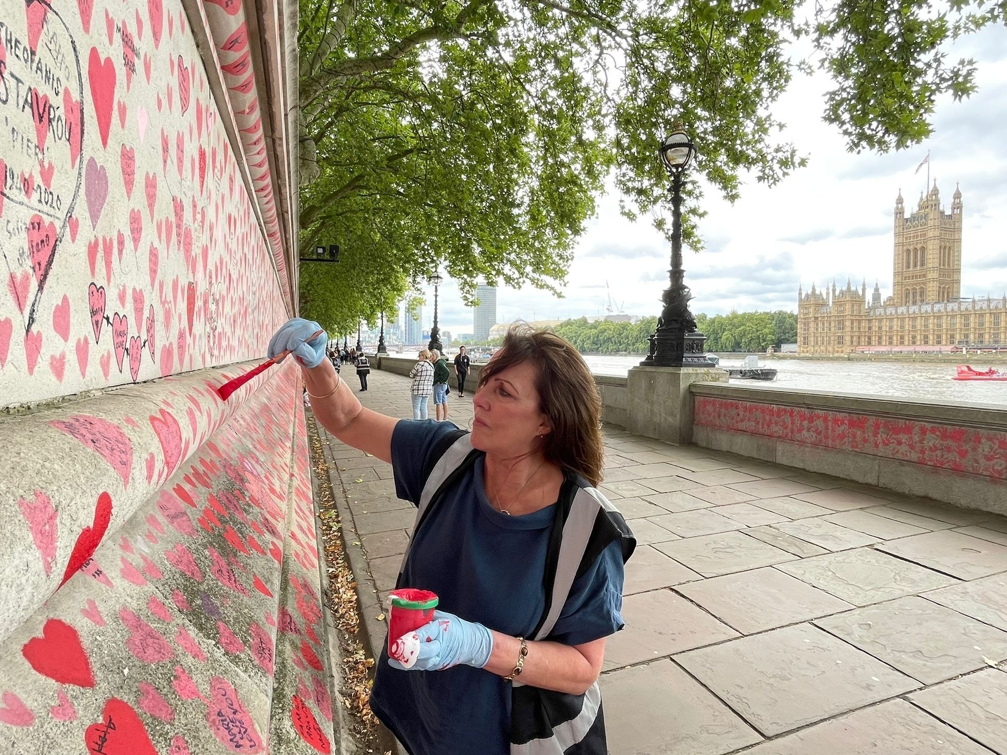 caption: Fran Hall paints hearts on a memorial in London dedicated to people who have died from COVID-19. She and other activists are pushing for the British government to investigate its handling of the pandemic.