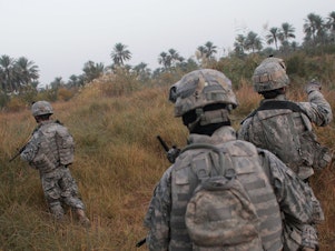caption: U.S. soldiers traverse fields on the way to conducting house-to- house searches in 2007 in Mukhisa, Iraq.