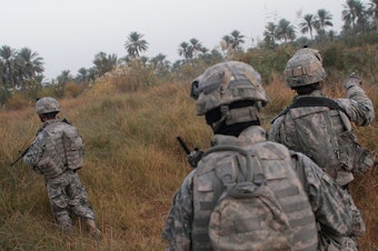 caption: U.S. soldiers traverse fields on the way to conducting house-to- house searches in 2007 in Mukhisa, Iraq.