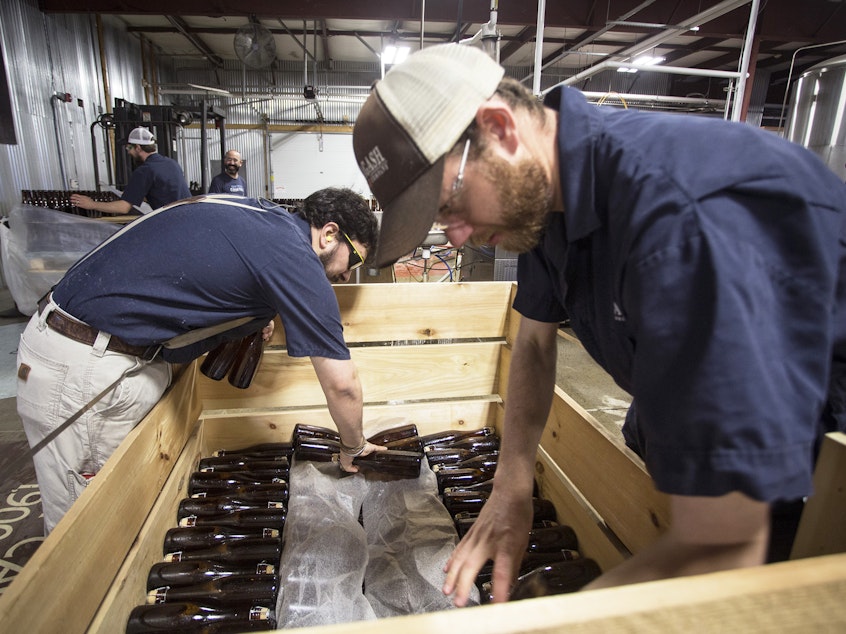 caption: Allagash employees Salim Raal, left, and Brendan McKay stack bottles of Golden Brett, a limited release beer fermented with a house strain of Brettanomyces yeast. The Maine brewery recently installed solar panels as part of its sustainability initiatives.