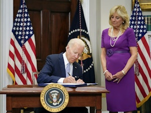 caption: President Biden signs into law the Bipartisan Safer Communities Act gun safety bill, in the Roosevelt Room of the White House on Saturday as first lady Jill Biden looks on.