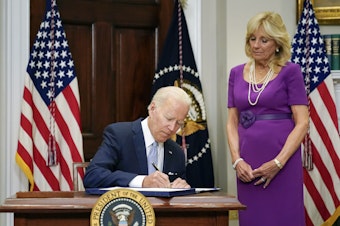 caption: President Biden signs into law the Bipartisan Safer Communities Act gun safety bill, in the Roosevelt Room of the White House on Saturday as first lady Jill Biden looks on.