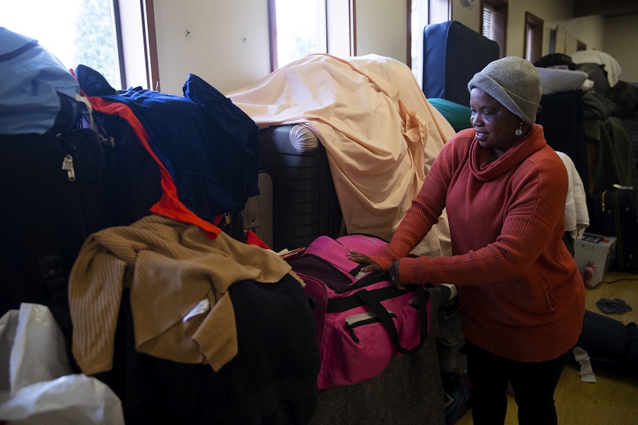 caption: Angela Joao Elisa, of Angola, retrieves an item from where her belongings are stored in a common area of the Riverton Park United Methodist Church, where nearly 200 people are sheltering while seeking asylum, on Monday, October 16, 2023, in Tukwila. 