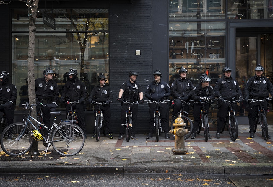 caption: FILE: Seattle police officers stand near the intersection of 5th and Pine Streets on Friday, November 24, 2017, during a Black Lives Matter rally in Seattle.