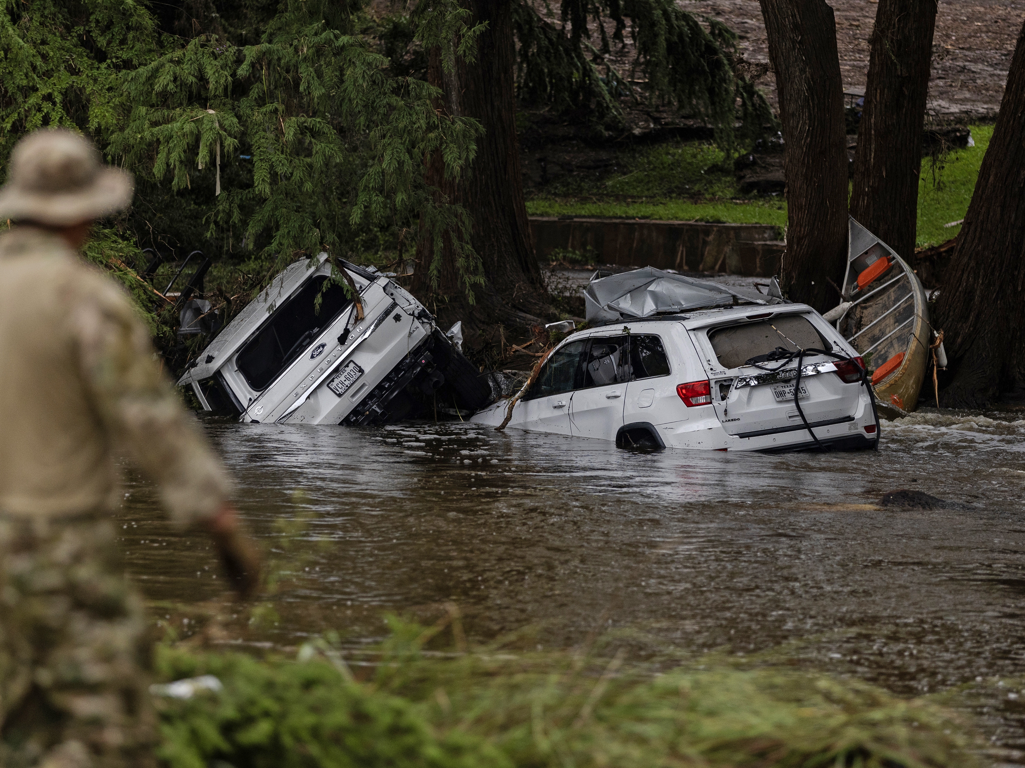 caption: Vehicles sit submerged as a search and rescue worker looks through debris from the early July flash flooding in Hunt, Texas.