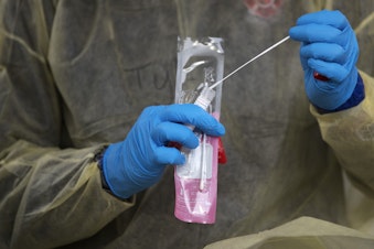 caption: Tyler Gachen, a firefighter with the Enumclaw Fire Department, puts a Covid-19 testing swab into a test tube after administering the test, on Wednesday, November 18, 2020, in the parking lot of the Weyerhaeuser King County Aquatic Center along Southwest Campus Drive in Federal Way. 