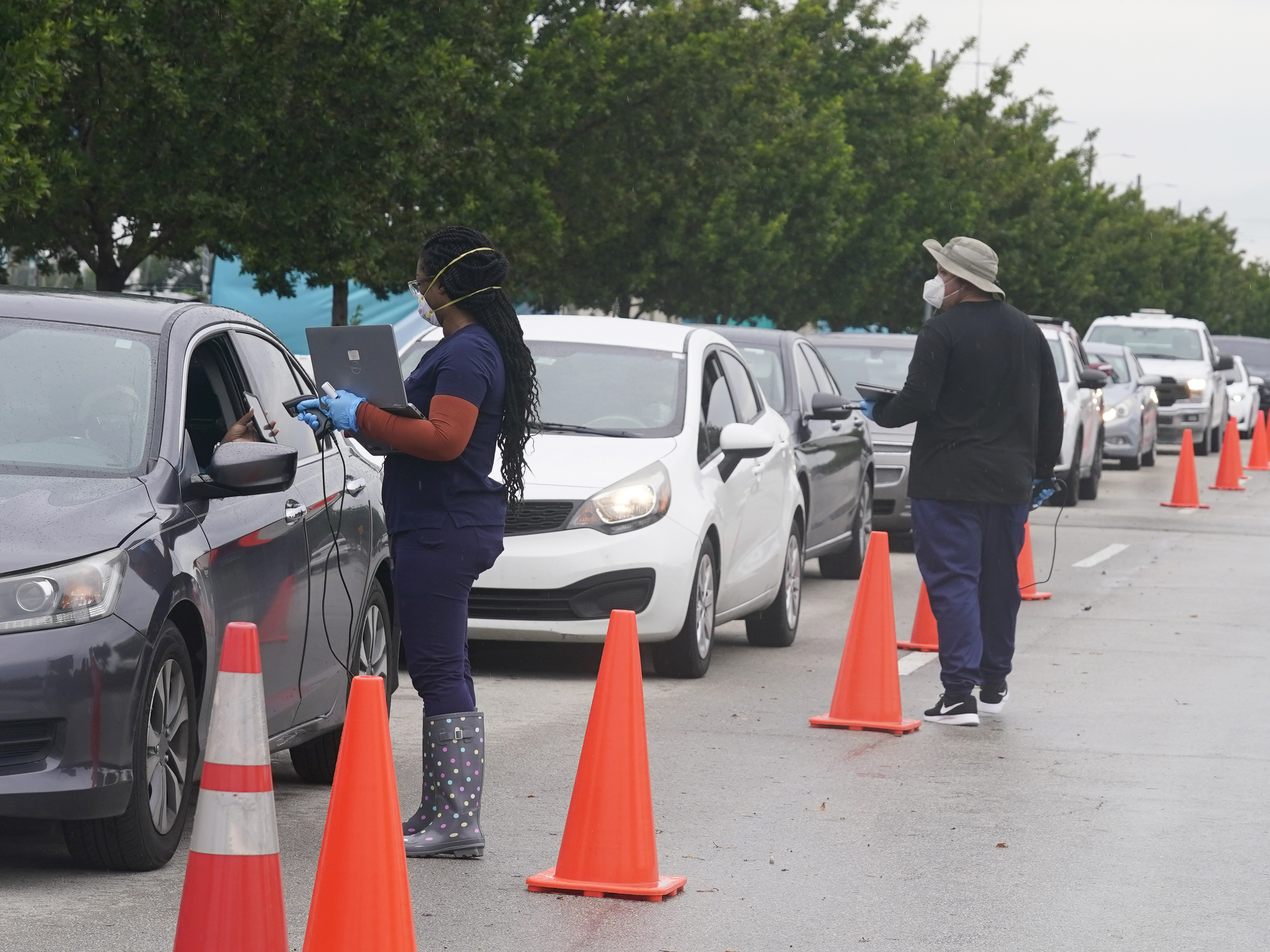 caption: Employees of Nomi Health check in a long line of people for COVID-19 tests on Tuesday in North Miami, Fla.