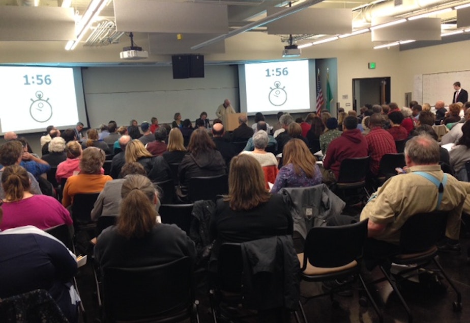 caption: Parents in a packed room listen to public testimony regarding proposed charter schools in the Seattle area at South Seattle Community College on Monday.