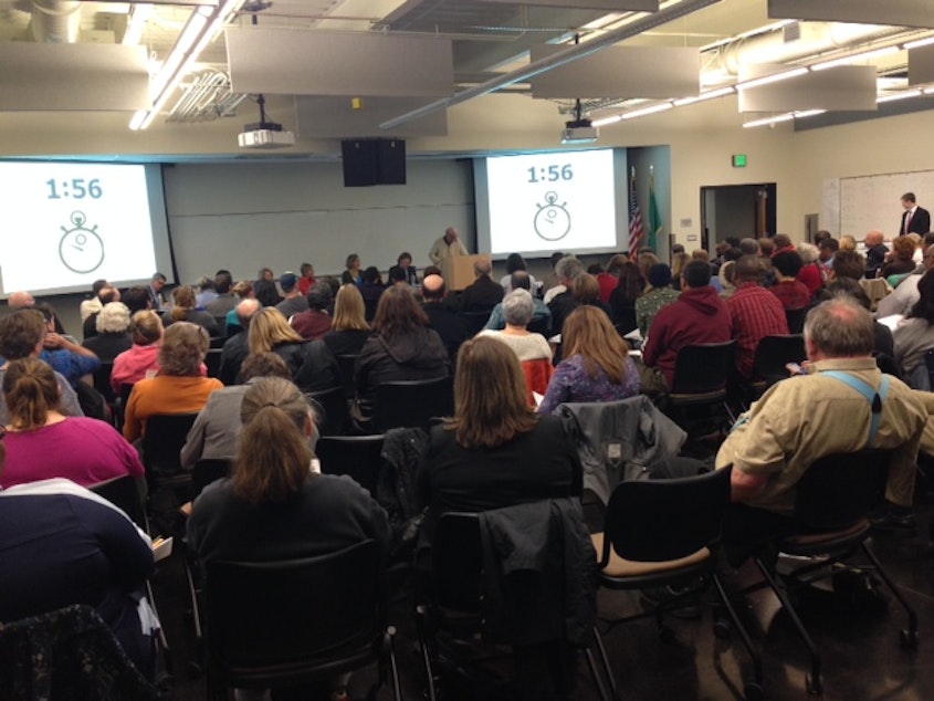 caption: Parents in a packed room listen to public testimony regarding proposed charter schools in the Seattle area at South Seattle Community College on Monday.