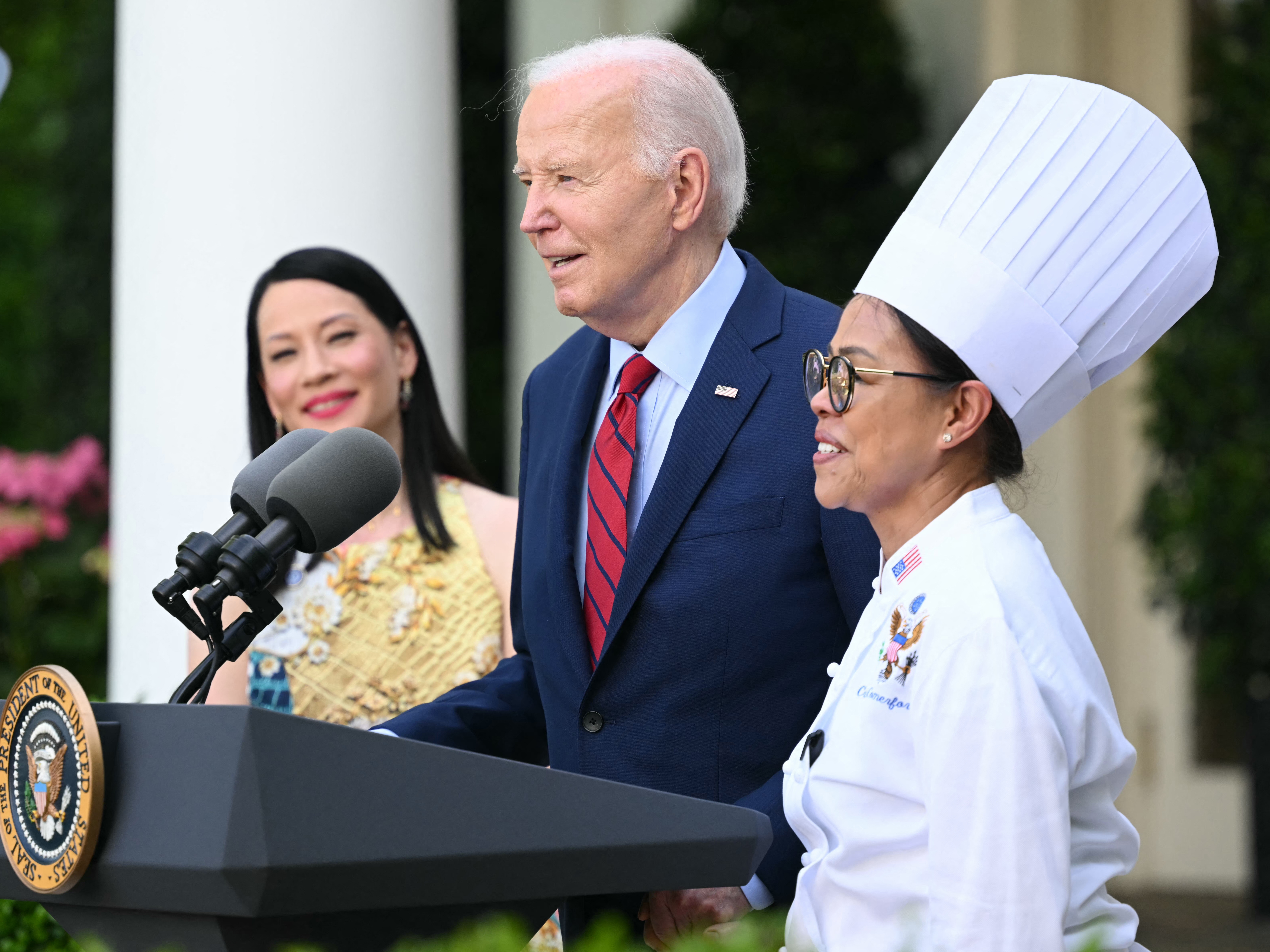 caption: President Biden welcomes then White House executive chef Cristeta Comerford to the podium during a reception celebrating Asian American, Native Hawaiian and Pacific Islander Heritage Month in May.