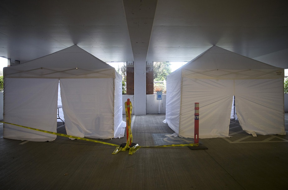 caption: White tents are set up in a parking garage of UW Northwest on Friday, March 6, 2020, in Seattle. Signs near the tents read 'Staff Testing.'