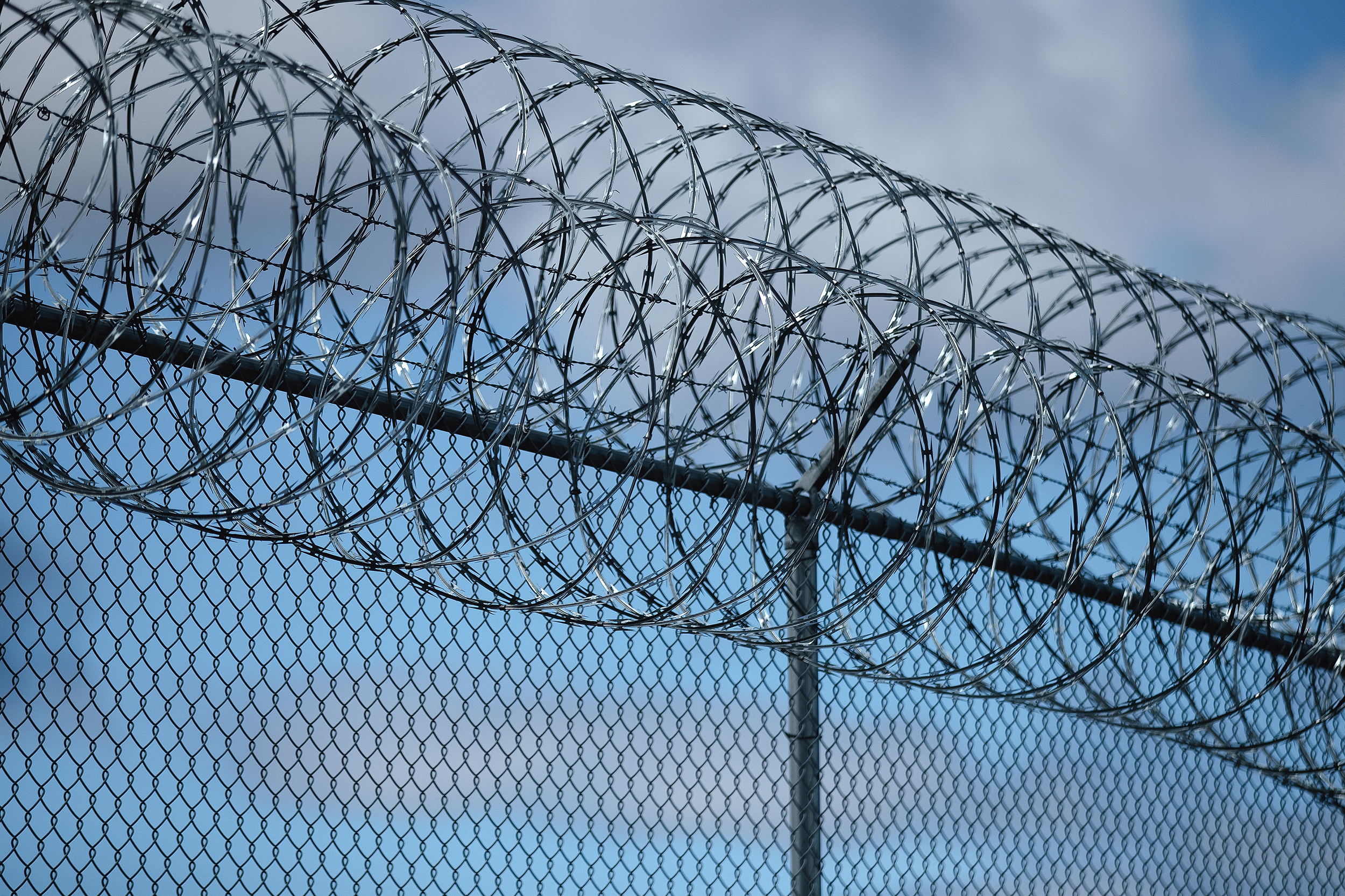 caption: Razor wire is shown near a crowd gathered for a solidarity day, led by La Resistencia, on Saturday, March 29, 2025, outside of the Northwest ICE Processing Center in Tacoma. 