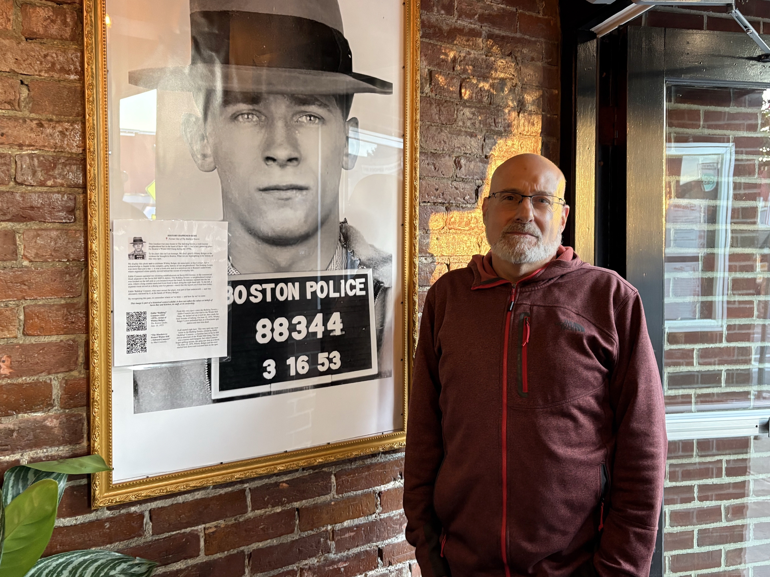 caption: The photo of Boston Mobster James Whitey Bulger looms large over Kenneth Osherow, co-owner of the Savin Bar + Kitchen in Boston. Osherow hung a page of "context" on the photo, explaining it was not meant to "celebrate" the mobster, but to "acknowledge a chapter in the gritty, complex history of the neighborhood."