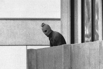 caption: A member of Black September appears on the balcony of the apartment where gunmen held members of the Israeli Olympic team hostage on Sept. 5, 1972. It was the first time a terrorist attack had been broadcast live to a global audience.