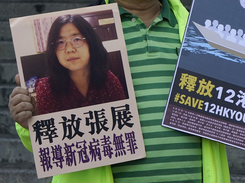 caption: A pro-democracy activist holds placards with the picture of Chinese citizen journalist Zhang Zhan outside the Chinese central government's liaison office, in Hong Kong, Monday. Activists demand the release of Zhang, as well as the 12 Hong Kong activists detained at sea by Chinese authorities.
