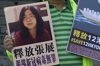 caption: A pro-democracy activist holds placards with the picture of Chinese citizen journalist Zhang Zhan outside the Chinese central government's liaison office, in Hong Kong, Monday. Activists demand the release of Zhang, as well as the 12 Hong Kong activists detained at sea by Chinese authorities.