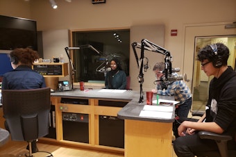 caption: RadioActive youth producers (left to right) Simone St. Pierre Nelson, Marian Mohamed, and Antonio Nevarez record the first youth-produced on-air showcase in December 2019 while RadioActive mentor Kyle Norris looks on.