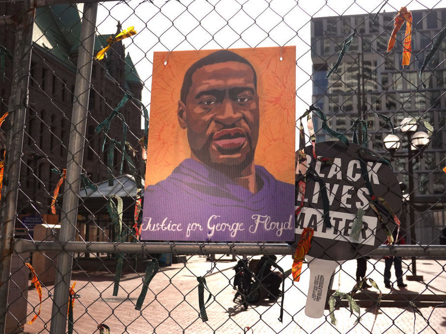 caption: A picture of George Floyd hangs on a fence barrier that surrounds the Hennepin County Government Center in Minneapolis on March 30. The Justice Department is bringing criminal charges against former police officer Derek Chauvin for allegedly violating Floyd's rights and using excessive force in restraining him.