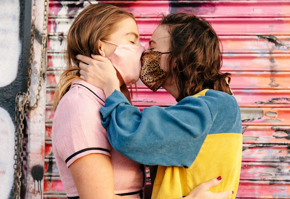 caption: Two people wearing face masks embrace and kiss