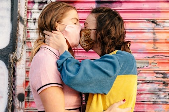 caption: Two people wearing face masks embrace and kiss