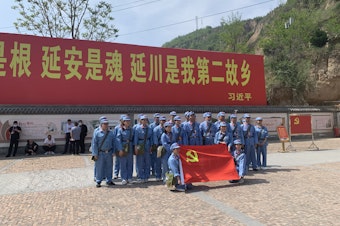 caption: Tourists dressed up as People's Liberation Army soldiers pose in Liangjiahe village, where a teenage Xi Jinping spent seven years doing hard labor. Today the village is a popular red tourism site. The sign displays a quote from Xi: "Liangjiahe is where my roots are, and my soul. It is my second home."