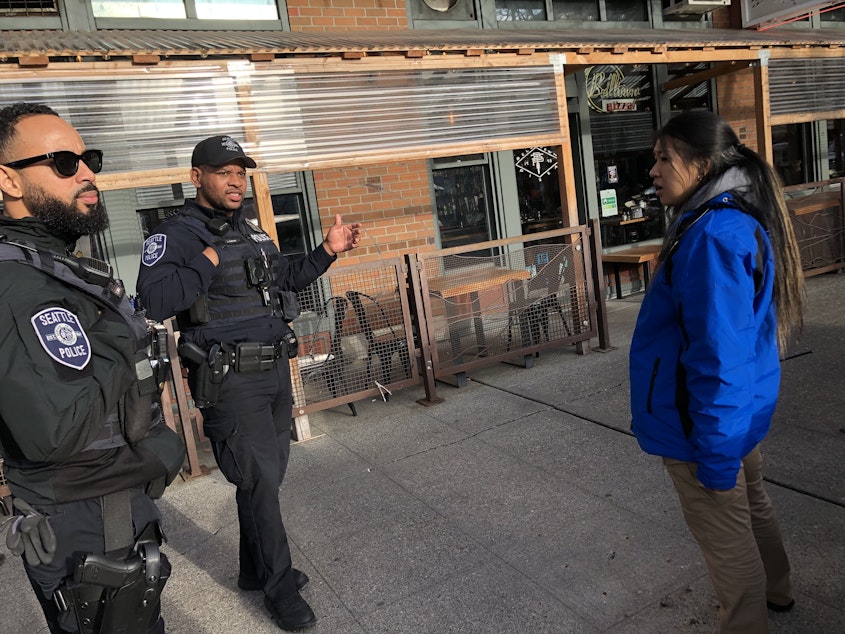 caption: Community crisis responder Sasha Pollock, right, checks in with Seattle police officers before approaching a crisis call in Seattle's Belltown neighborhood in December 2023. 