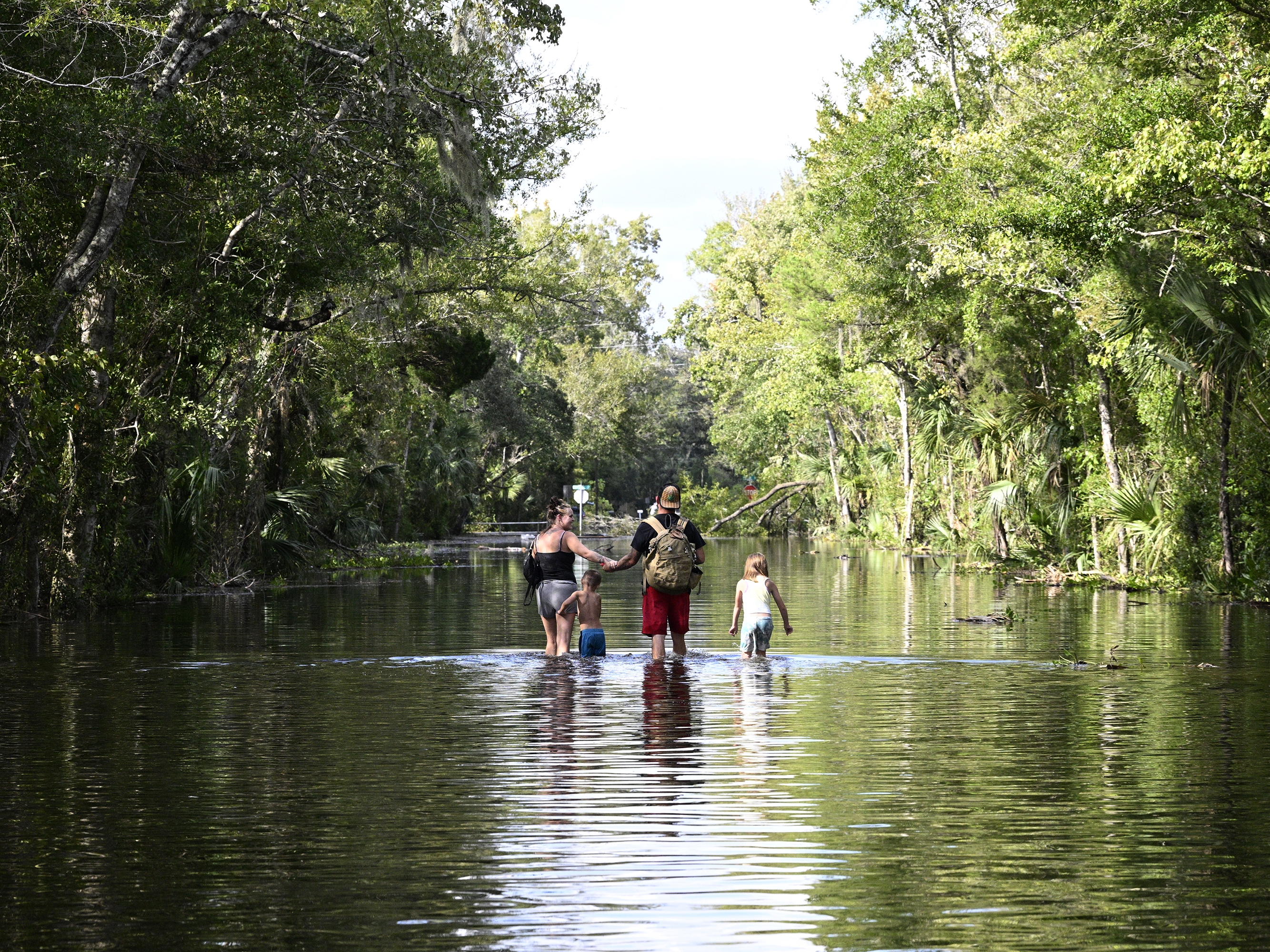caption: Dustin Holmes, second from right, holds hands with his girlfriend, Hailey Morgan, while returning to their flooded home with her children Aria Skye Hall, 7, right, and Kyle Ross, 4, in the aftermath of Hurricane Helene, Friday, Sept. 27, 2024, in Crystal River, Fla.