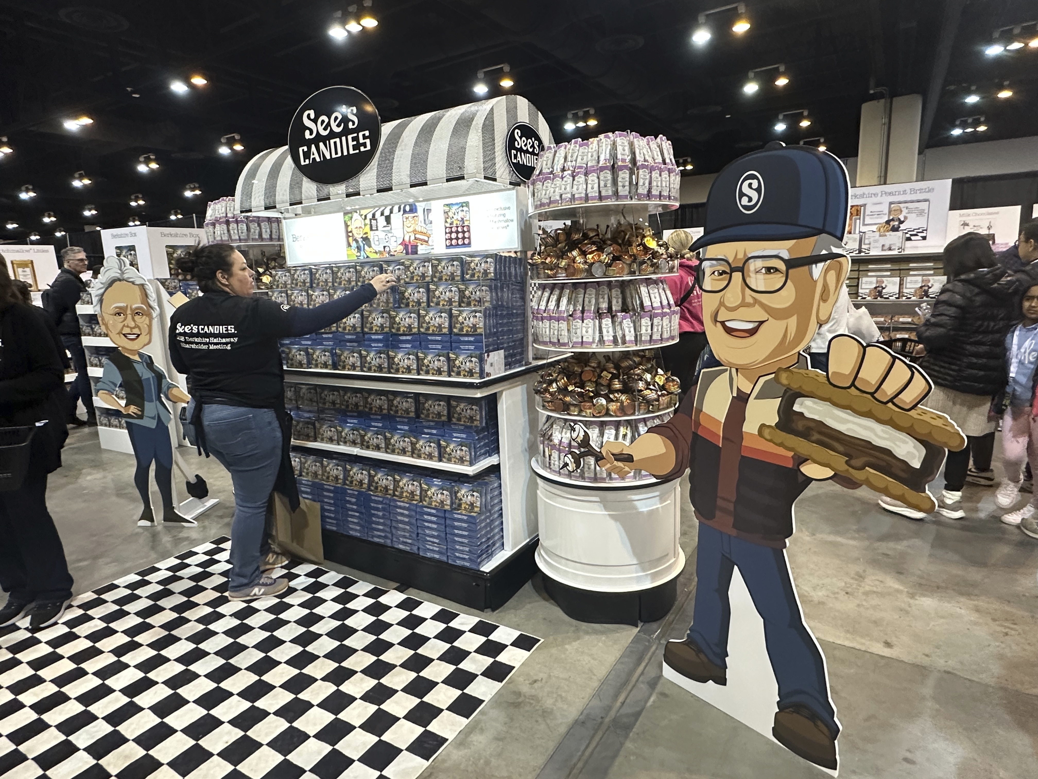 caption: A See's Candies worker restocks the display next to a cutout of Warren Buffett at the Berkshire Hathaway shareholders meeting exhibit hall Friday, May 2, 2025 in Omaha, Neb. (AP Photo/Josh Funk)