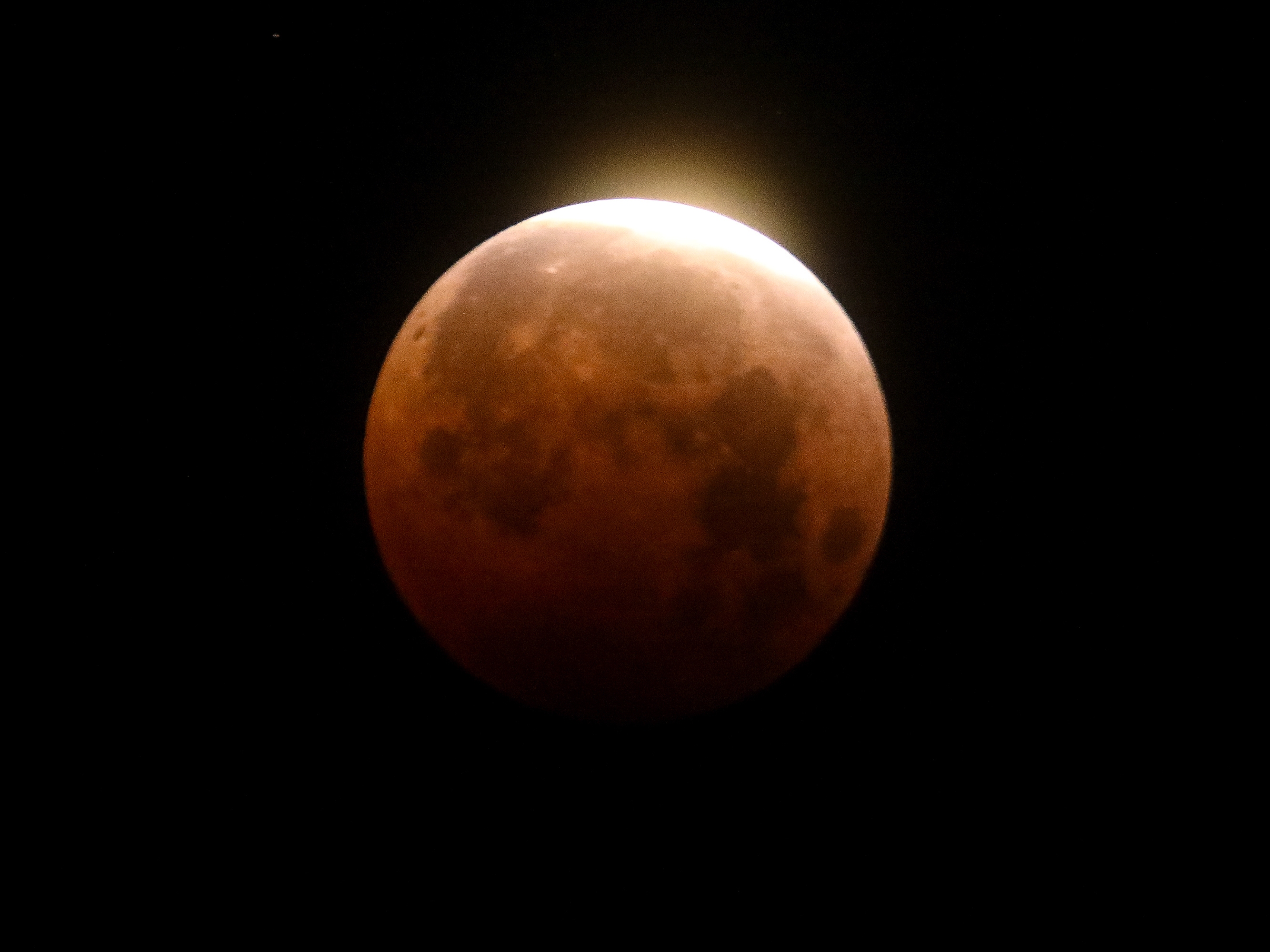 caption: Light shines from a total lunar eclipse over Santa Monica Beach in California in 2021.