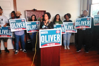 caption: Nikkita Oliver, surrounded by supporters, declares 3rd place in Seattle's mayoral race a victory.