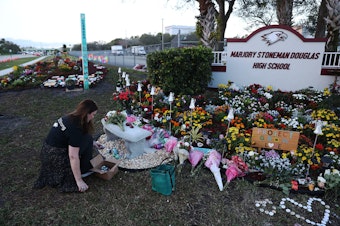 caption: PARKLAND, FLORIDA - FEBRUARY 14:  Suzanne Devine Clark visits a memorial setup at Marjory Stoneman Douglas High School for those killed during a mass shooting on February 14, 2019 in Parkland,  Florida. A year ago on Feb. 14th at Marjory Stoneman Douglas High School 14 students and three staff members  were killed during the mass shooting. (Photo by Joe Raedle/Getty Images)