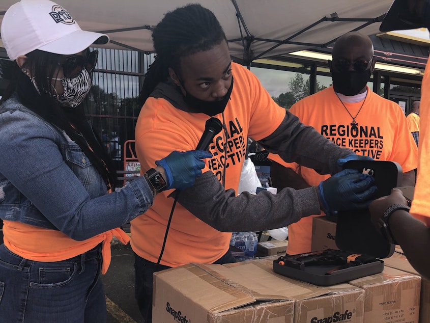 caption: Aaron Knox, center, with the YMCA's Alive & Free program, demonstrates how to use a firearm lockbox at the June 4, 2021 kickoff of King County's Regional Peacekeepers Collective in Skyway.