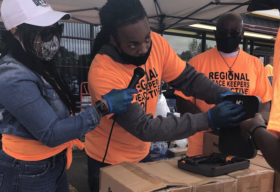 caption: Aaron Knox, center, with the YMCA's Alive & Free program, demonstrates how to use a firearm lockbox at the June 4, 2021 kickoff of King County's Regional Peacekeepers Collective in Skyway.