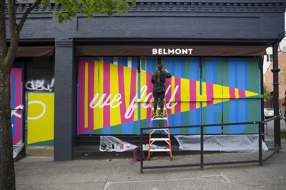 caption: Sara Thompson paints a mural on Sunday, May 3, 2020, at the intersection of East Pike Street and Belmont Avenue in Seattle. When complete, the mural will read "United we stand, divided we fall."