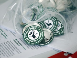 caption: Pro-union pins sit on a table during a watch party for Starbucks' employees union election in December in Buffalo, N.Y. Starbucks union organizers say the company is closing a New York store to retaliate.