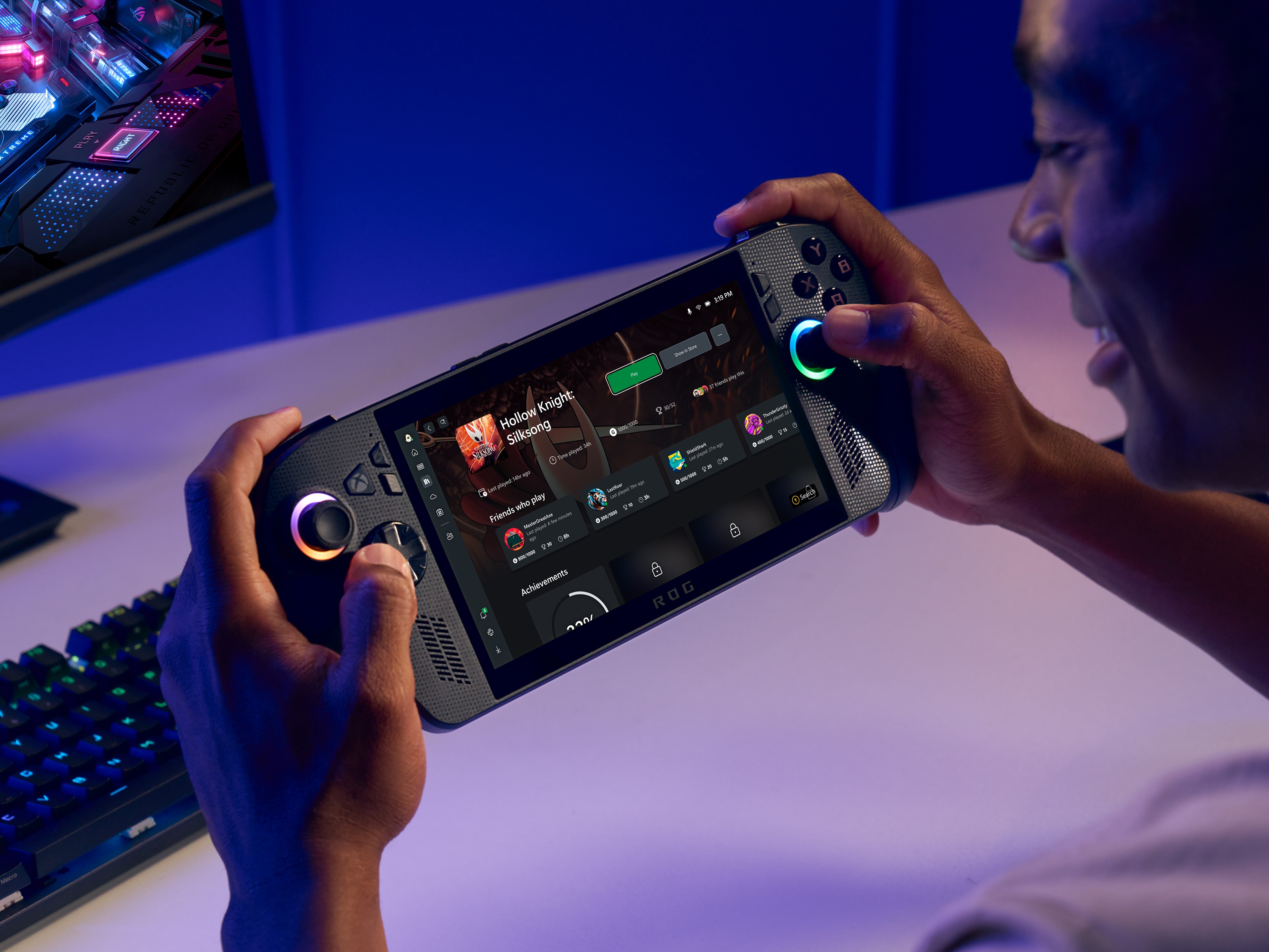 caption: A promotional image for the ROG Xbox Ally X, demonstrating the handheld PC with a full gaming desktop nearby.
