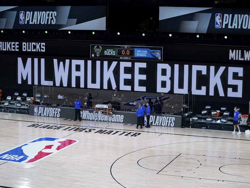 caption: Officials stand beside an empty court at the scheduled start of an NBA basketball playoff game between the Milwaukee Bucks and the Orlando Magic, Wednesday in Lake Buena Vista, Fla. The Bucks didn't take the floor in protest against racial injustice and the shooting of Jacob Blake, a Black man, by police in Kenosha, Wisconsin.