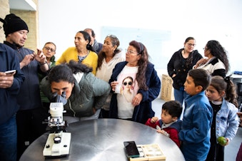 caption: Salamanca, joined by her grandkids at the end of science class, wait their turn to look through a microscope.