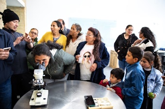 caption: Salamanca, joined by her grandkids at the end of science class, wait their turn to look through a microscope.