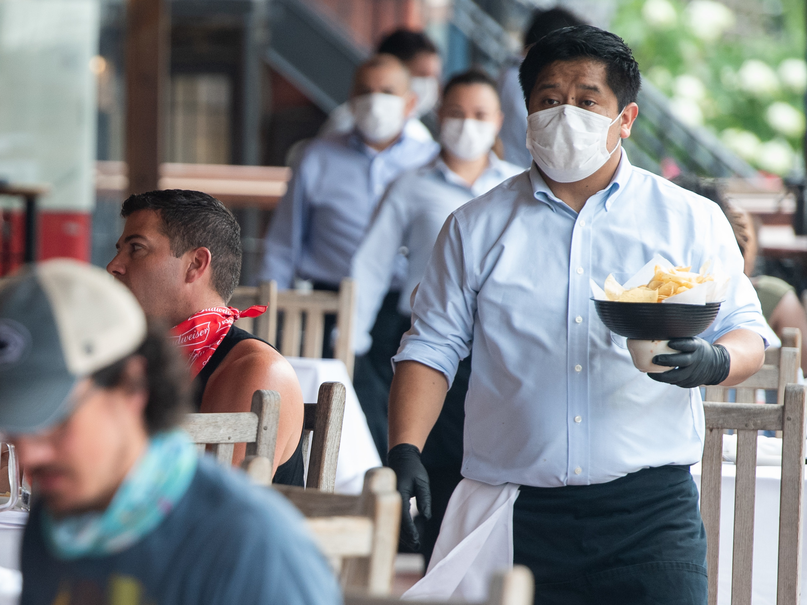 A waiter wearing a mask and gloves delivers food to a table to customers seated at an outdoor patio at a Mexican restaurant in Washington, DC, May 29, 2020.